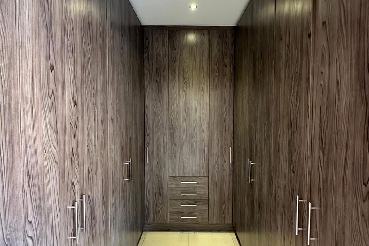 A well-appointed walk-in closet featuring extensive floor-to-ceiling dark wood cabinetry with integrated storage drawers and recessed ceiling lighting.