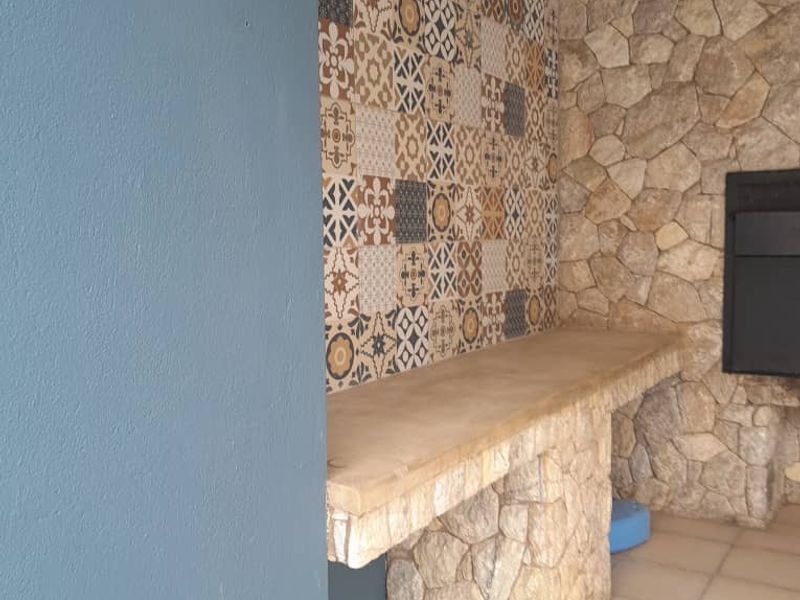 Covered patio area featuring a built-in braai, stone-clad base, decorative tiled splashback, and a concrete countertop.