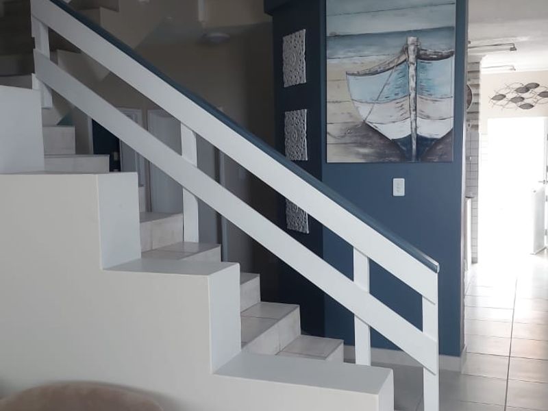 A bright hallway featuring a staircase with white railings and tiled flooring, leading towards an open living area.
