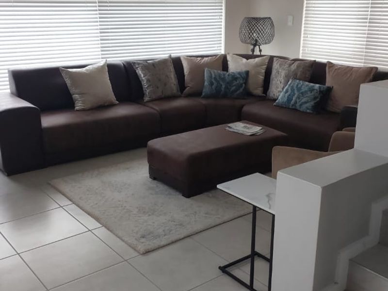 A well-lit living room featuring neutral tiled flooring, large windows with venetian blinds, and a staircase leading to the upper level.