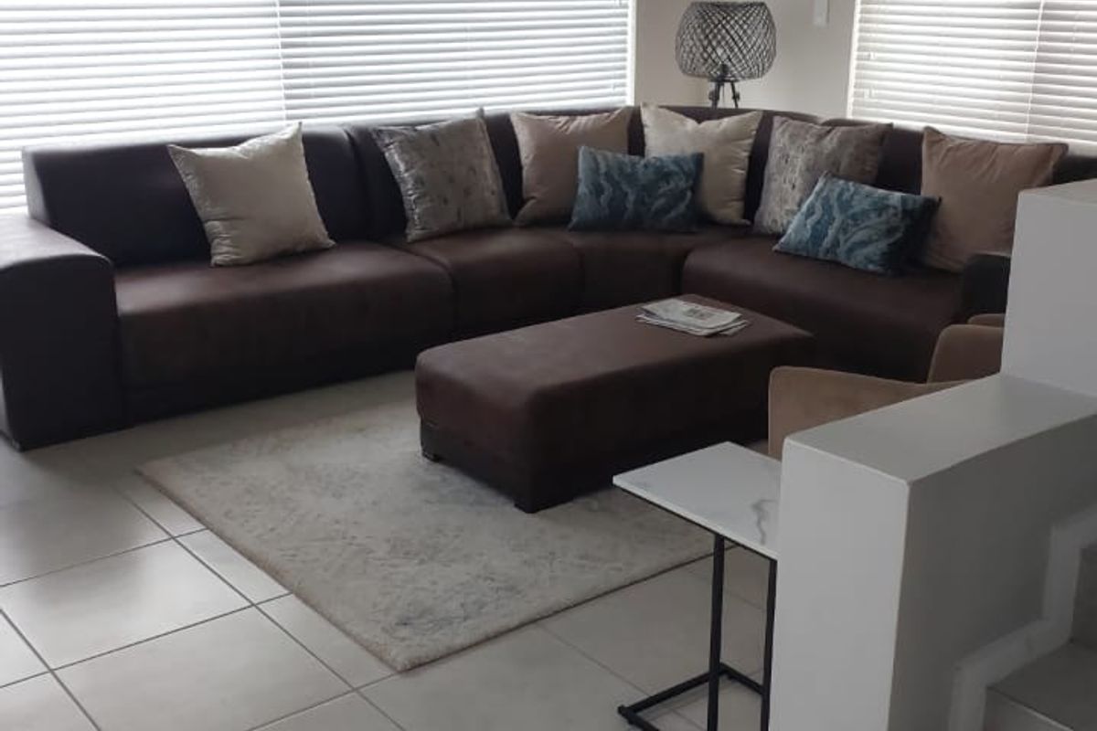 A well-lit living room featuring neutral tiled flooring, large windows with venetian blinds, and a staircase leading to the upper level.