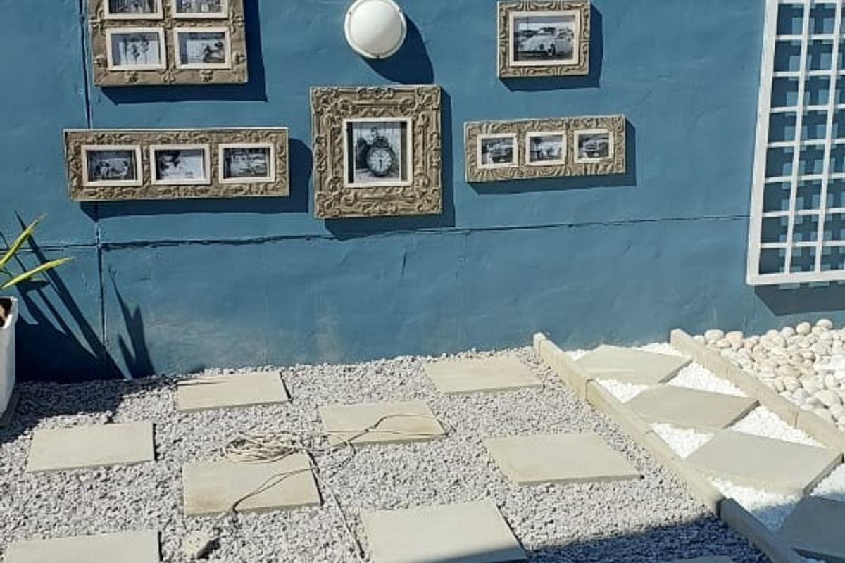 A rear courtyard area featuring a blue painted boundary wall with integrated lighting, decorative trellis, and a low-maintenance gravel and paver landscape design.