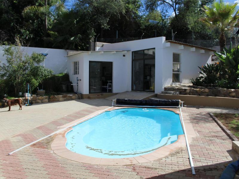 Outdoor pool area featuring a swimming pool with a cover, paved surround, and a detached outbuilding with glass sliding doors.