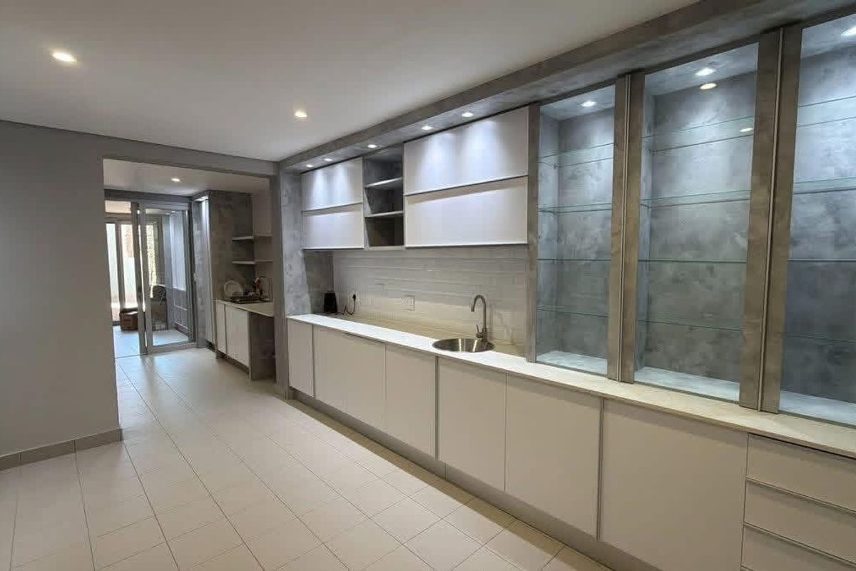 Modern kitchen featuring sleek white cabinetry, integrated glass display shelving with accent lighting, tiled flooring, and a clean, minimalist aesthetic.