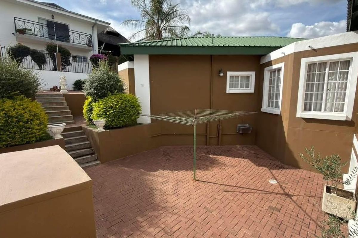 A private rear courtyard featuring brick paving, concrete stairs leading to an upper level, and well-maintained exterior walls.