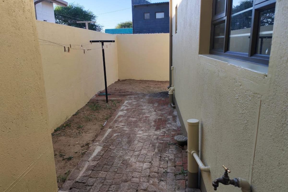 A side courtyard area featuring brick paving, a perimeter boundary wall, and an external water tap.