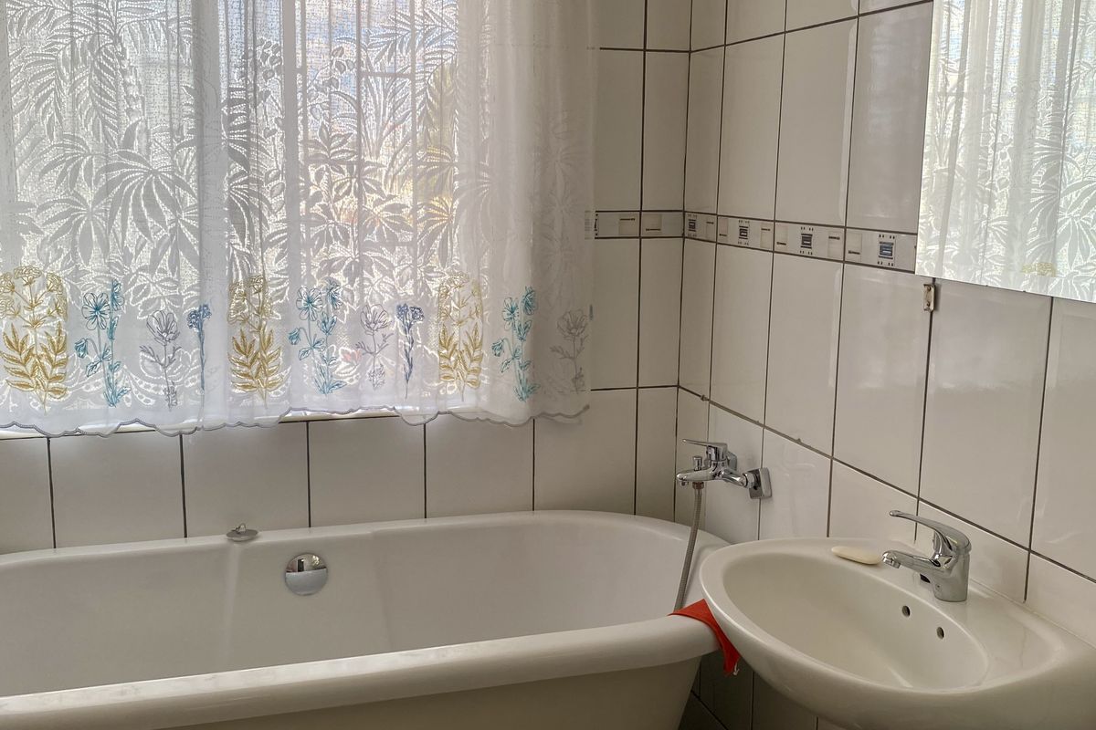 A functional bathroom featuring a standard bathtub, wall-mounted basin, and tiled walls, offering a clean and practical space.
