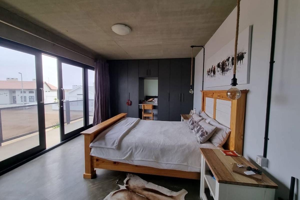 Modern bedroom featuring an exposed concrete ceiling, dark built-in cabinetry with a vanity nook, and large sliding glass doors leading to an outdoor area.