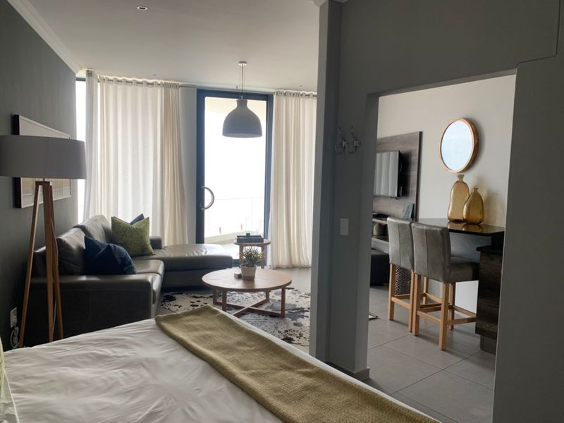 Open plan living area featuring tiled flooring, recessed ceiling lighting, and large glass sliding doors leading to a balcony with natural light.