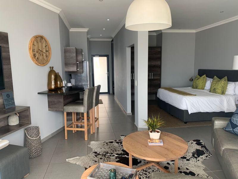 An open-plan studio apartment featuring a compact kitchenette with built-in cabinetry, tiled flooring, and a combined living and sleeping area.