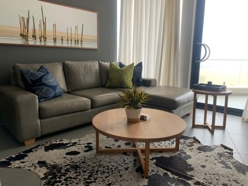 A modern living room featuring large glass sliding doors leading to a balcony, neutral tiled flooring, and a contemporary grey feature wall.