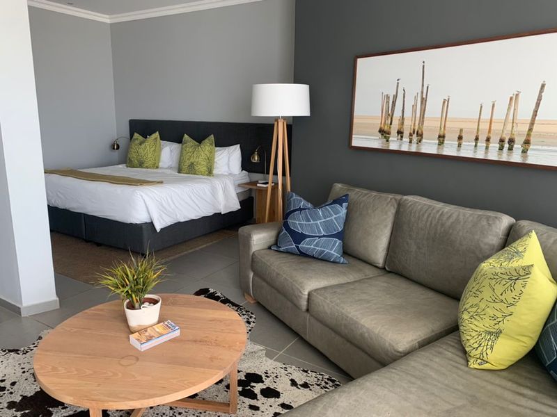 A spacious open-plan bedroom and living area featuring modern neutral finishes, tiled flooring, and a contemporary accent wall.