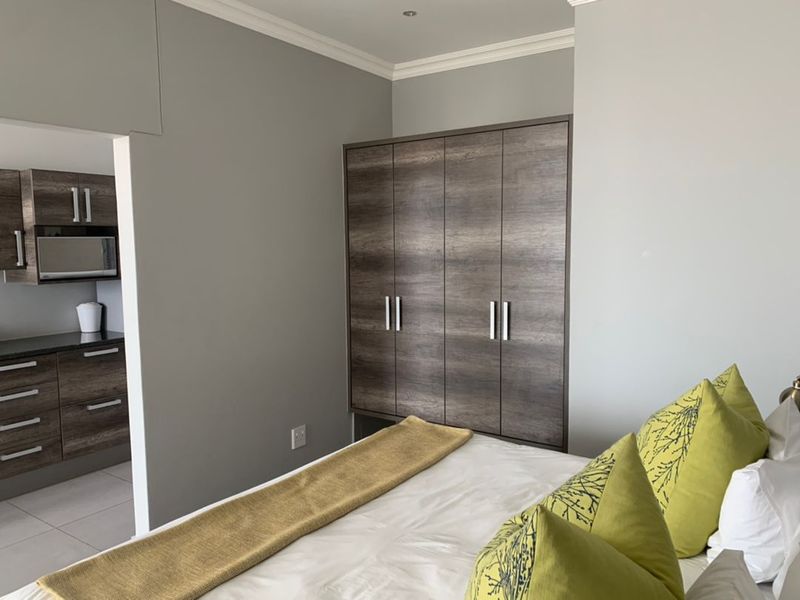 A bedroom featuring built-in wooden cabinetry, with a view into an adjacent kitchen area with matching cabinetry and modern finishes.