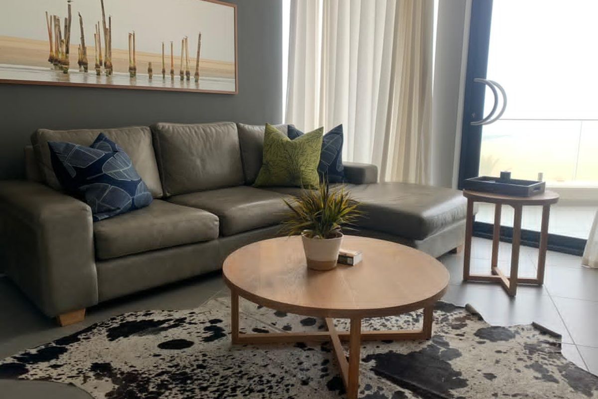 A modern living room featuring large glass sliding doors leading to a balcony, neutral tiled flooring, and a contemporary grey feature wall.