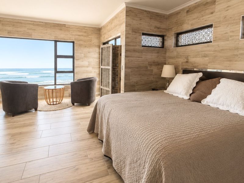 Spacious bedroom featuring wood-look tile flooring, wall cladding, and large windows offering expansive ocean views.