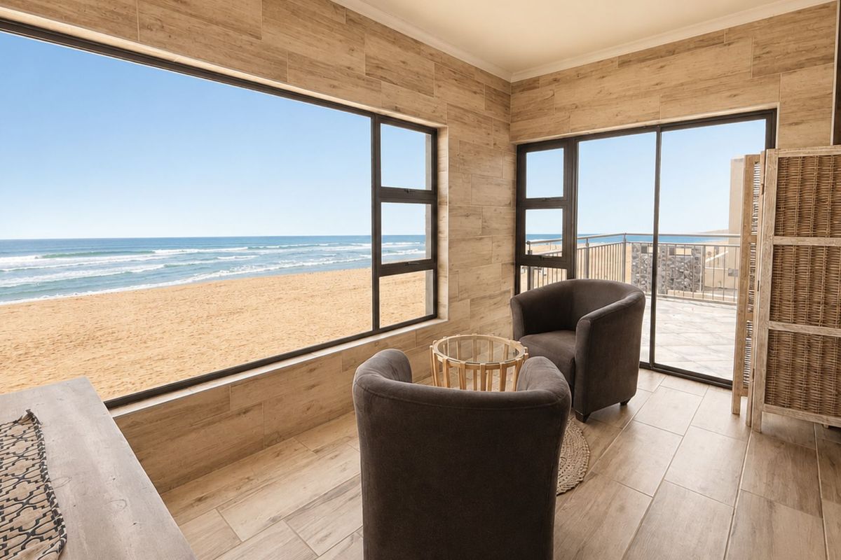 A bright living area featuring wood-look tile flooring, large picture windows, and sliding glass doors leading to a balcony with direct ocean views.