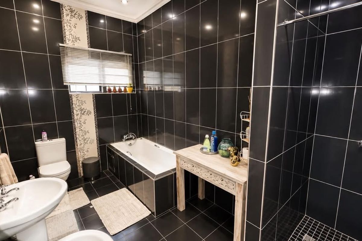 A modern bathroom featuring black wall and floor tiles, a built-in bathtub, a separate shower enclosure, and a pedestal basin.