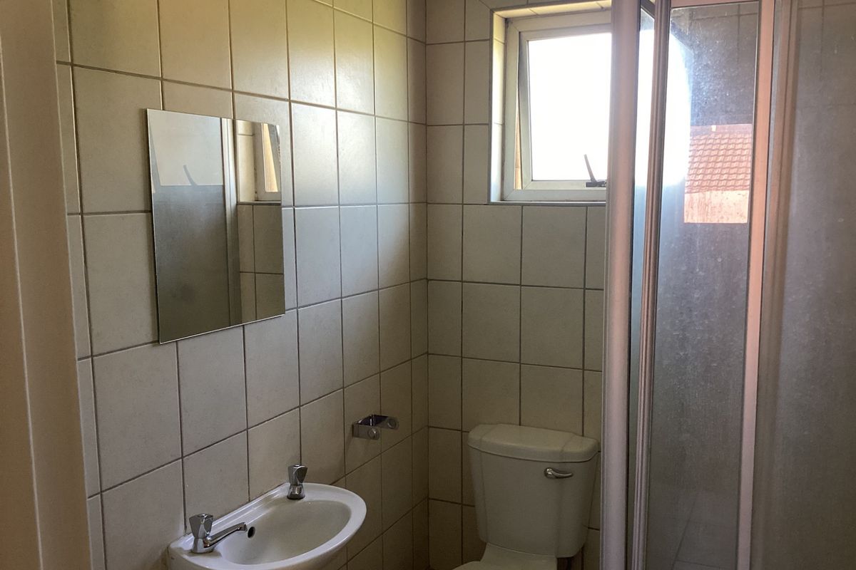 A compact bathroom featuring a shower enclosure, a wall-mounted basin, and a toilet, finished with neutral wall tiling and a small window.