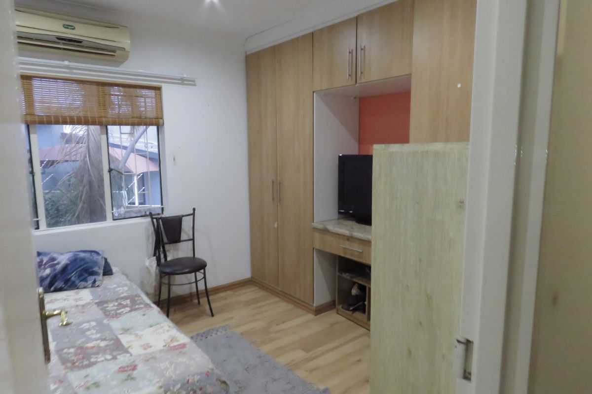 A bedroom featuring laminate flooring, built-in cupboards with an integrated desk area, and a wall-mounted split-system air conditioner.