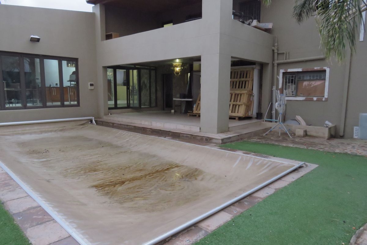 Rear exterior view featuring a covered patio, swimming pool with cover, and artificial lawn area, showing signs of wear and maintenance requirements.