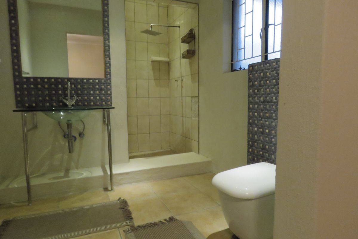 A functional bathroom featuring a walk-in shower with a rain shower head, a wall-mounted toilet, and a modern glass vessel sink.