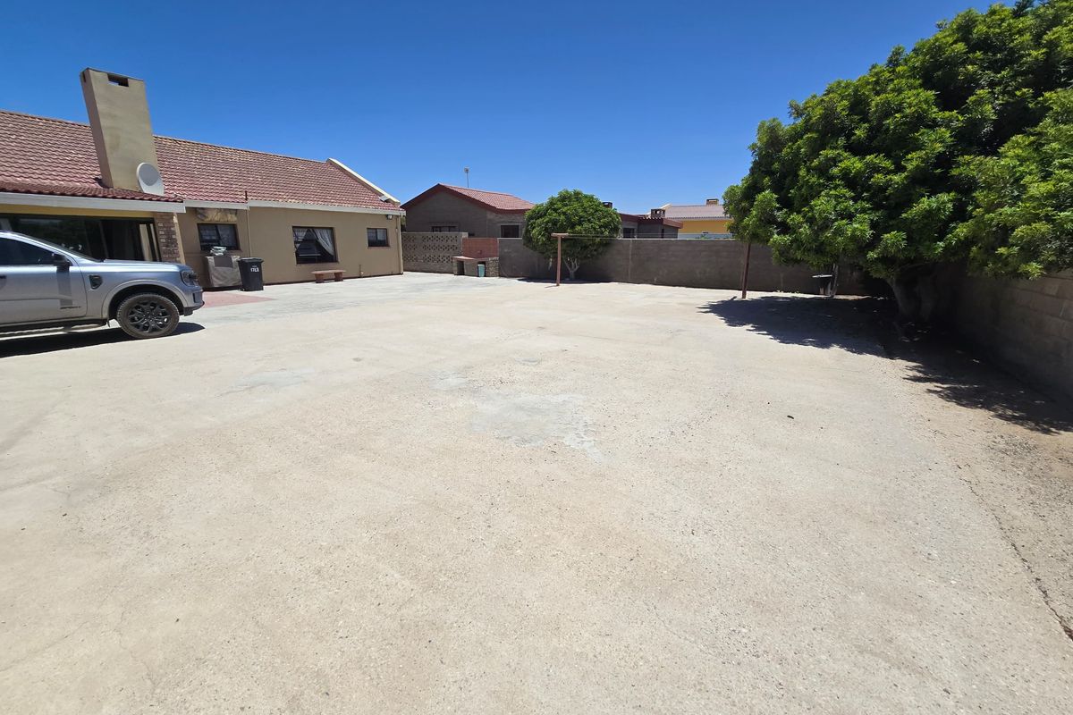 A spacious rear exterior area featuring a large concrete paved yard, perimeter boundary walls, and a built-in outdoor braai area.