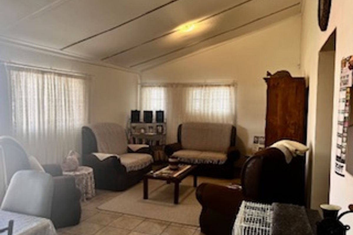 A spacious living room featuring a raked ceiling, tiled flooring, and large windows that provide ample natural light.