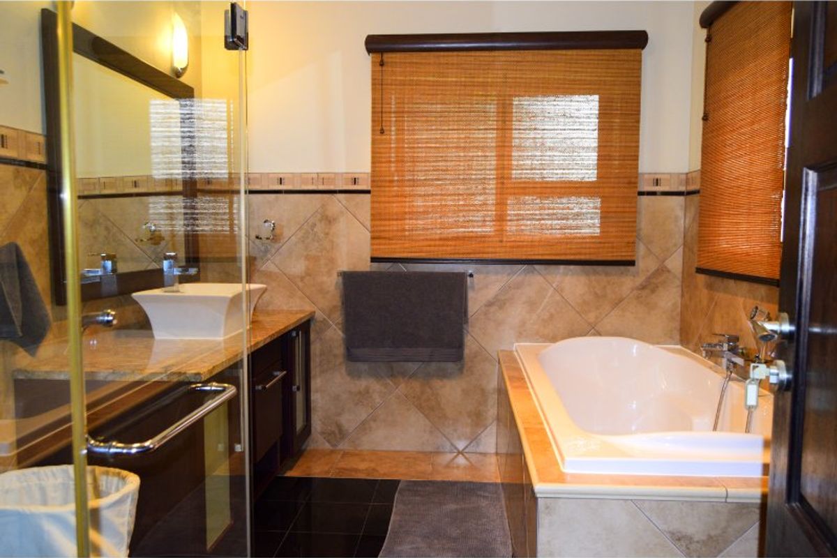 A well-appointed bathroom featuring a vessel sink on a granite vanity, a glass-enclosed shower, and a built-in bathtub with neutral ceramic tiling.