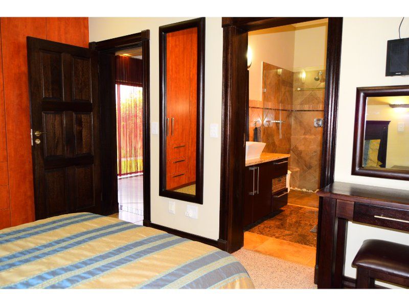 Bedroom featuring dark timber door frames, built-in cabinetry, and an adjoining en-suite bathroom with a shower and vanity basin.