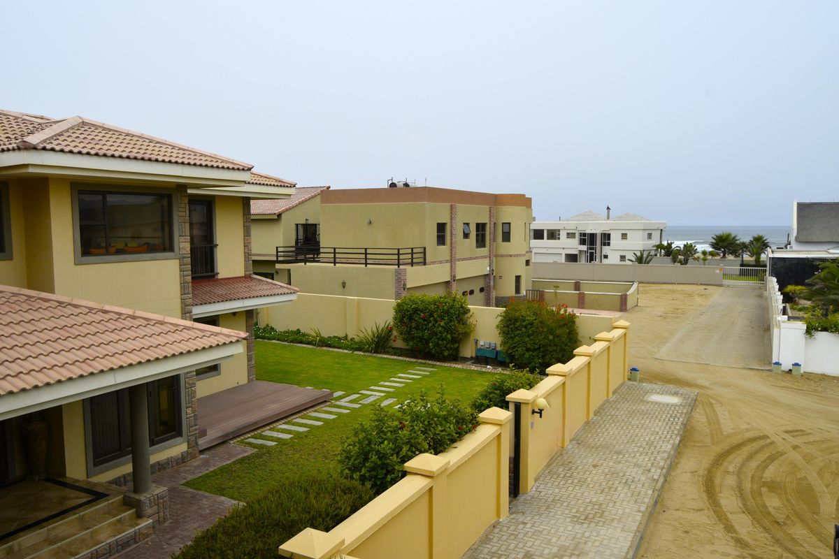 Rear view of the property featuring a landscaped garden, timber deck, and secure boundary wall with paved access.