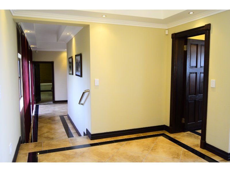 A spacious hallway featuring tiled flooring with a decorative border, recessed ceiling lighting, and dark wood door frames leading to adjacent rooms.
