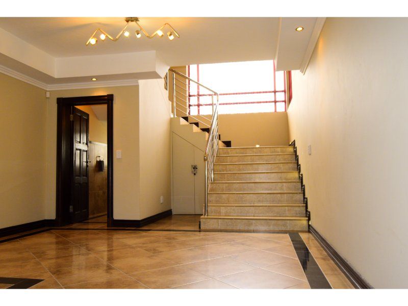 Spacious entrance hall featuring tiled flooring with a decorative border, a staircase with a stainless steel balustrade, and convenient under-stair storage.