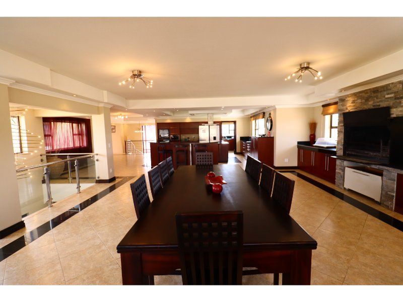 Spacious open-plan living and dining area featuring a stone fireplace, modern kitchen cabinetry, and a glass balustrade overlooking the lower level.