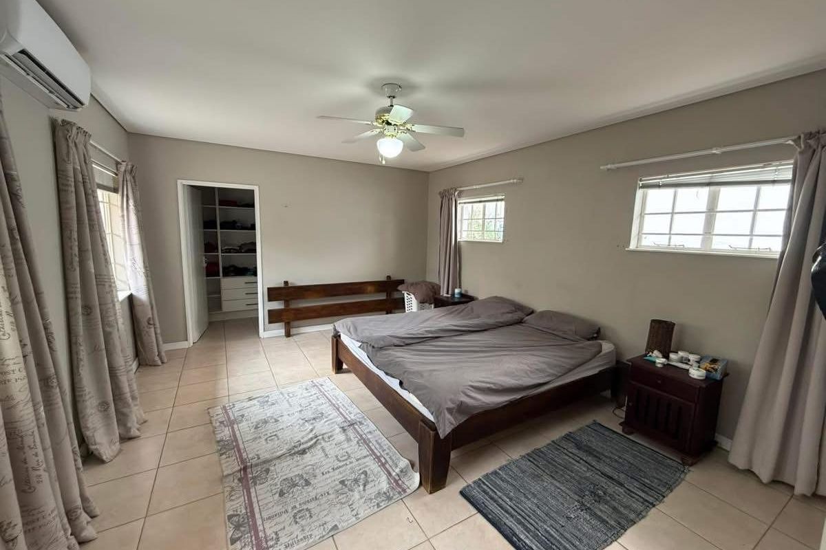 Spacious bedroom featuring tiled flooring, a ceiling fan, wall-mounted air conditioning unit, and an integrated walk-in closet area.