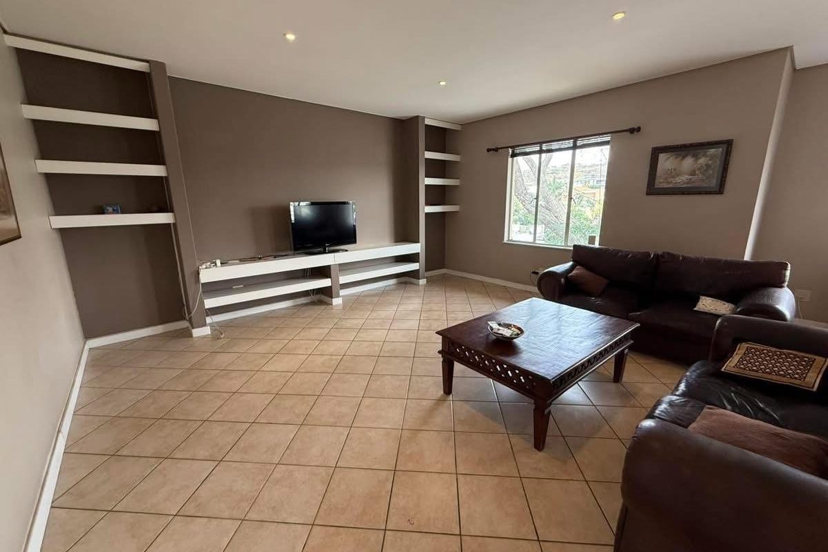 Spacious living room featuring built-in shelving units, tiled flooring, and recessed ceiling lighting, offering a functional and comfortable living space.