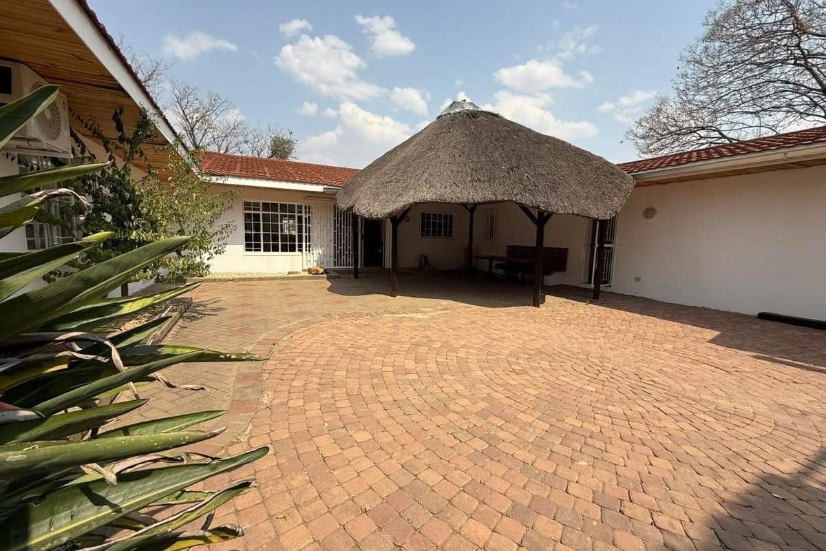 Spacious rear courtyard featuring a traditional thatched lapa, paved flooring, and direct access to the main house structure.