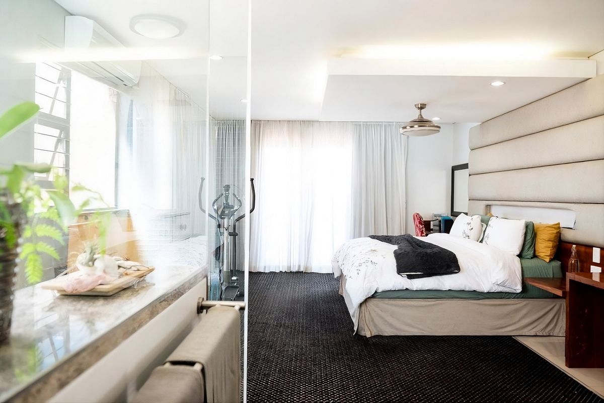 Spacious bedroom featuring a modern upholstered headboard, recessed ceiling lighting, and an integrated glass-enclosed bathroom area with contemporary finishes.