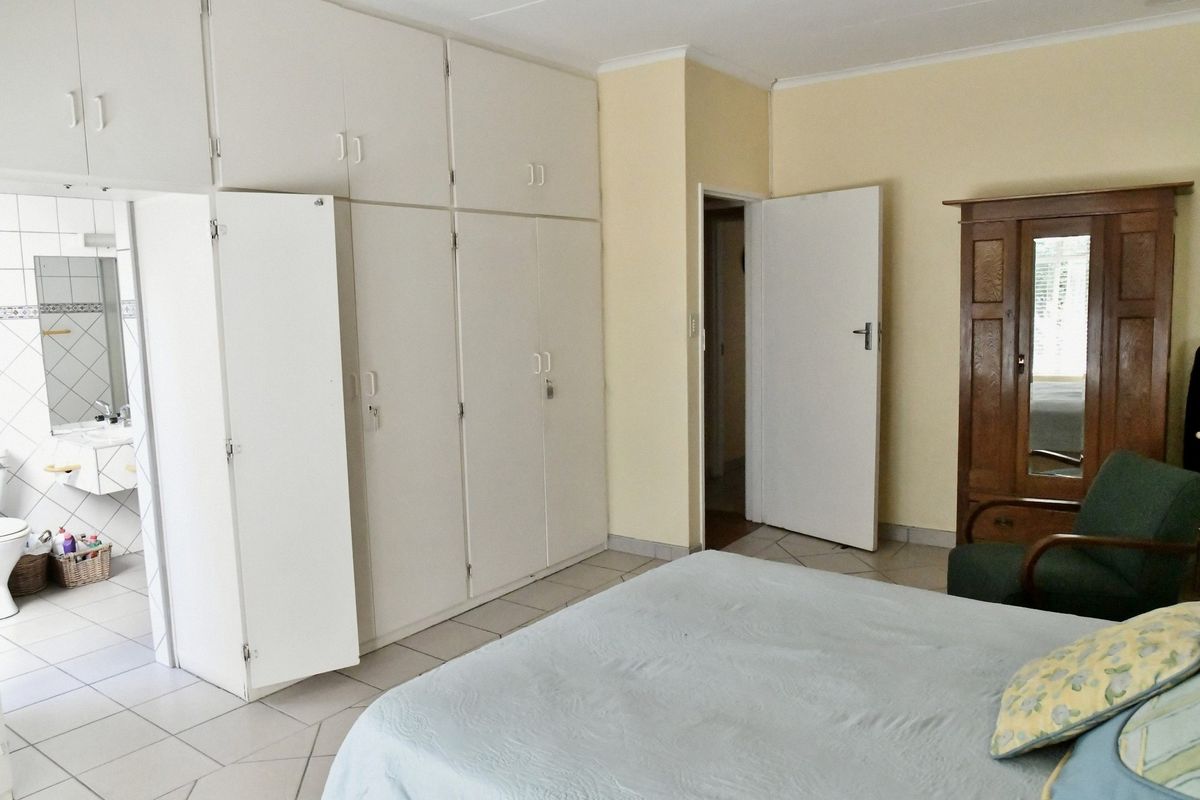 Bedroom featuring built-in floor-to-ceiling cupboards and tiled flooring, with an adjoining en-suite bathroom visible through the doorway.