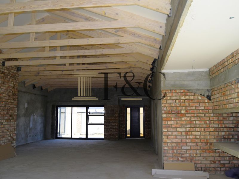 Spacious open-plan living area under construction, featuring exposed timber roof trusses, brick feature walls, and large aluminium sliding doors leading to the exterior.