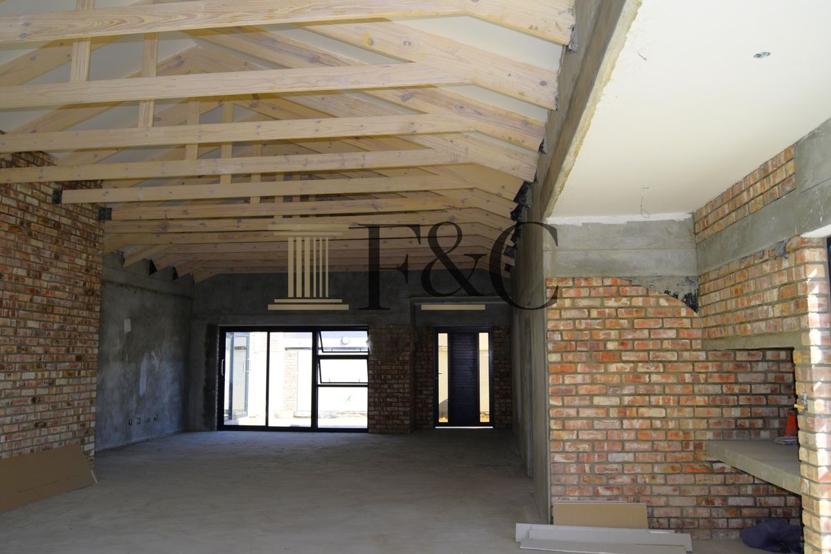 Spacious open-plan living area under construction, featuring exposed timber roof trusses, brick feature walls, and large aluminium sliding doors leading to the exterior.