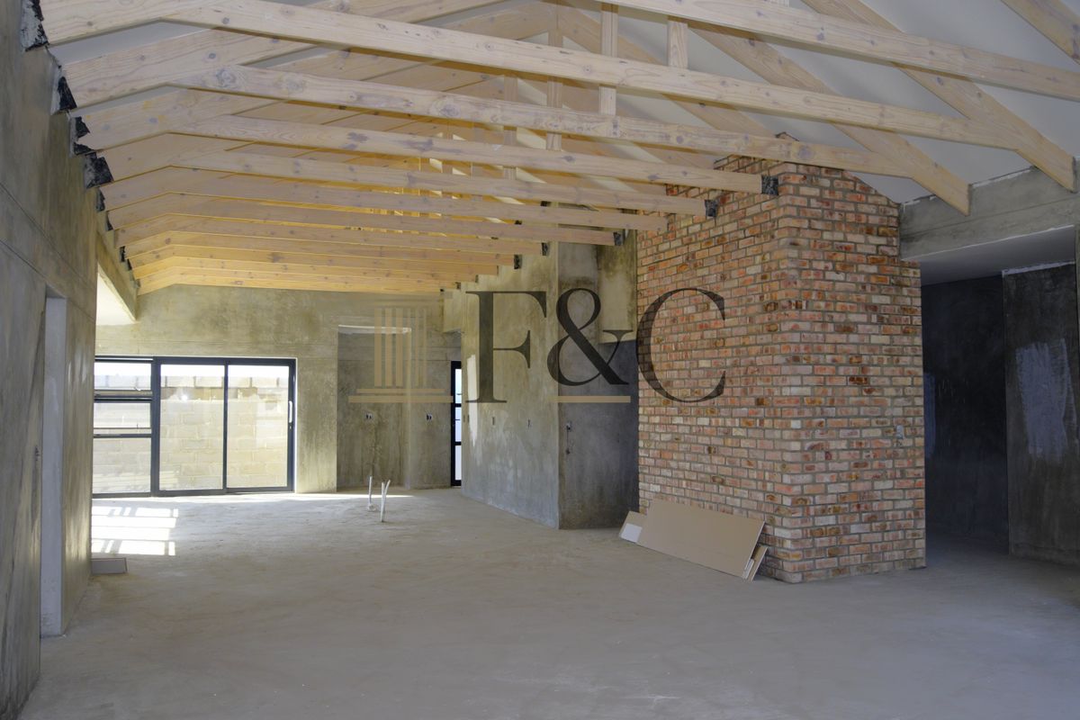 Spacious open-plan interior under construction, featuring exposed timber roof trusses, a prominent brick chimney breast, and large sliding glass doors.