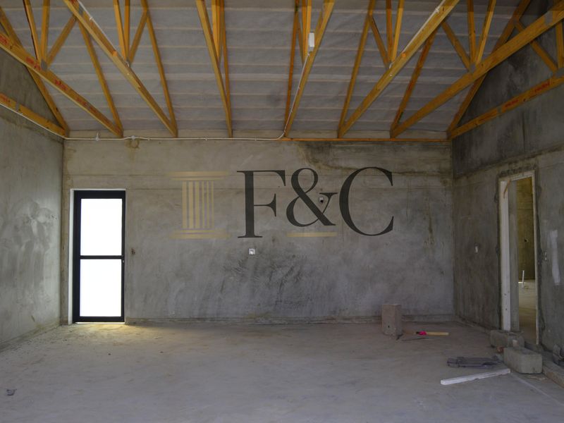 An unfinished open-plan interior space featuring exposed timber roof trusses, raw concrete walls, and cement flooring, currently in a shell construction state.