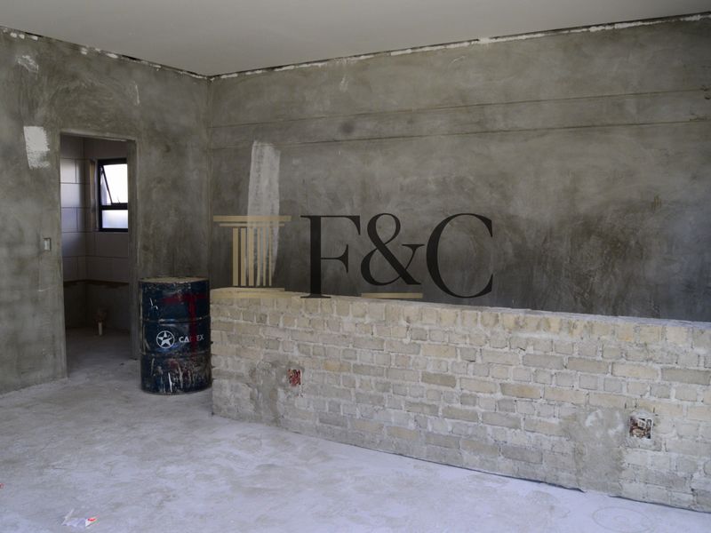 An unfinished open-plan living area featuring raw plastered walls, exposed brickwork, and cement flooring, currently in a shell condition awaiting final finishes.
