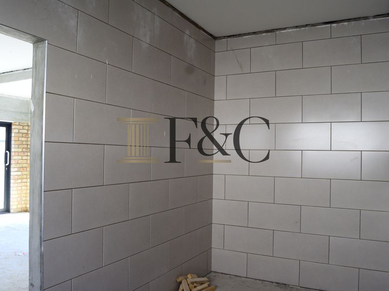An unfinished interior space featuring grey ceramic wall tiles and an aluminium door frame, currently in a construction phase.