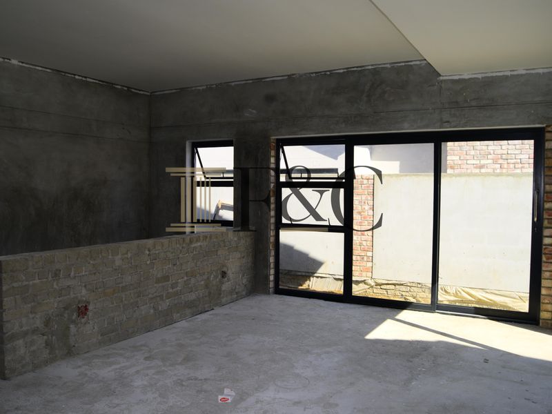 An unfinished living area featuring exposed brickwork, cement plaster walls, and large sliding glass doors leading to the exterior.