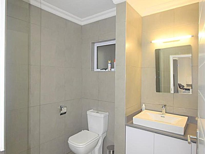 Modern bathroom featuring a wall-mounted vanity with basin, a toilet, and a glass-enclosed shower with neutral floor-to-ceiling tiling.