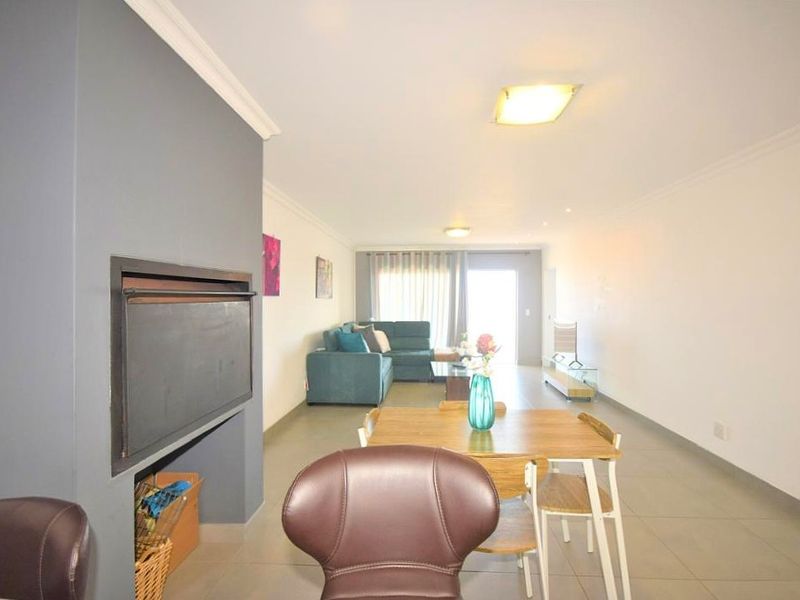 Spacious open-plan living and dining area featuring a built-in fireplace, neutral tiled flooring, and direct access to an outdoor balcony through sliding doors.