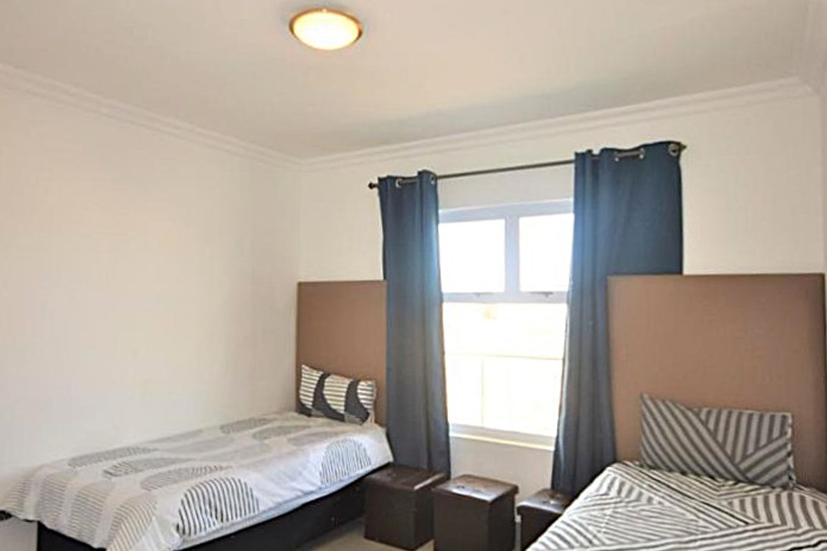 A functional bedroom featuring tiled flooring, a central ceiling light, and a window with curtain rod.