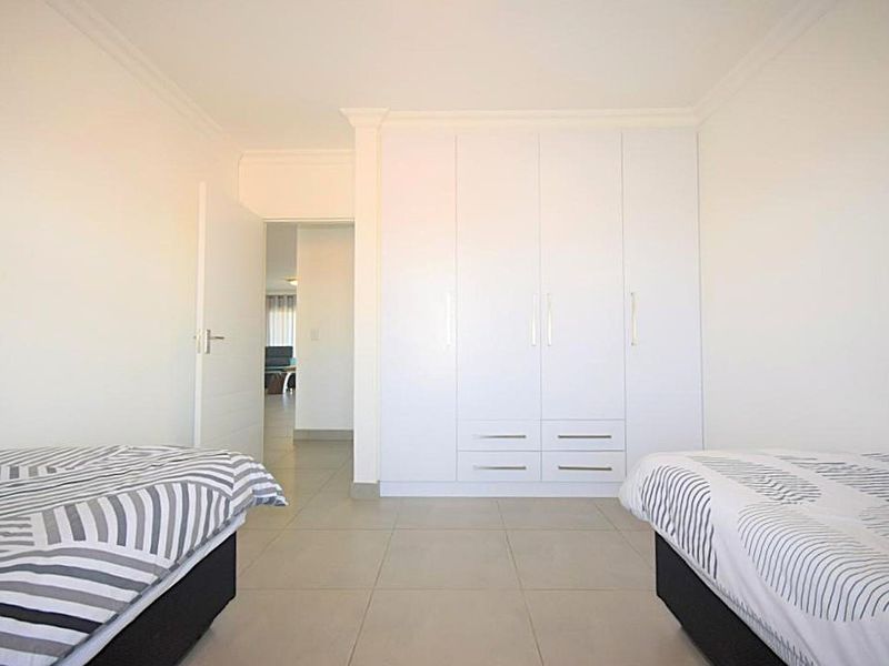 A clean, bright bedroom featuring neutral tiled flooring and ample built-in cupboard storage with a modern finish.