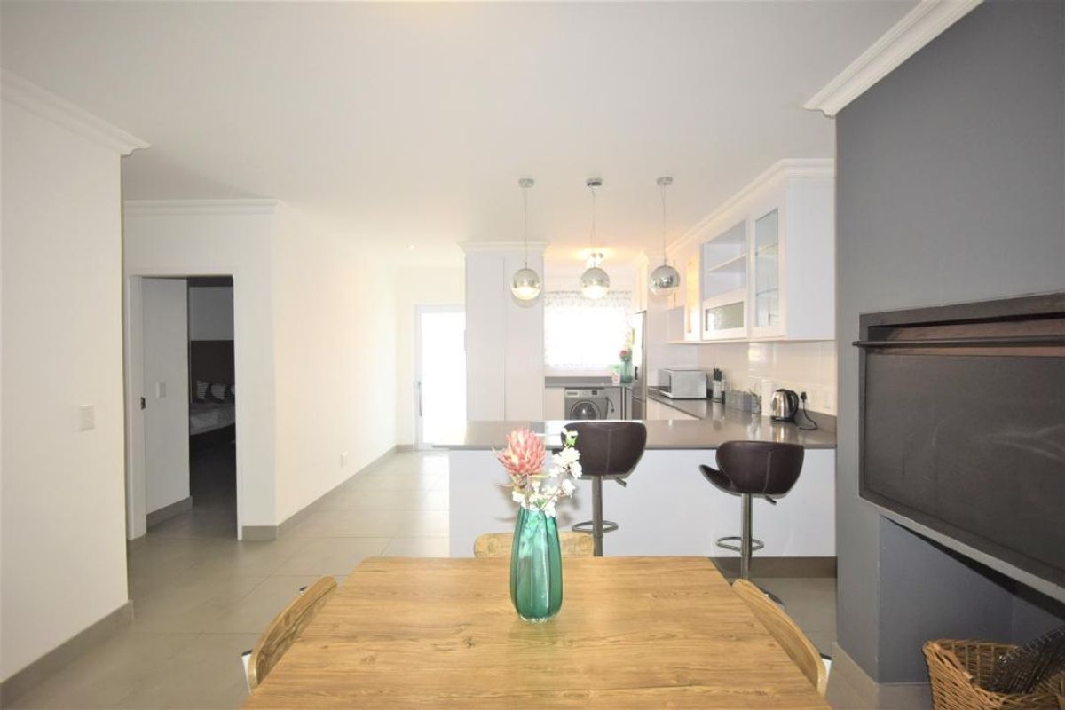 Open-plan living and kitchen area featuring modern cabinetry, stone countertops, a breakfast bar, and a built-in fireplace with tiled flooring throughout.